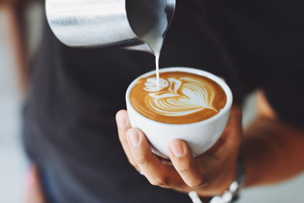 pexels-photo-302899 Close-up of a barista pouring milk to create latte art in a coffee cup.